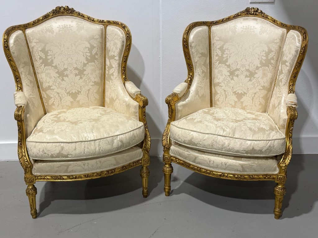 Pair of Louis XV Style Giltwood Bergeres: Fine pair of Louis XV style bergère armchairs featuring richly carved giltwood frames with floral cresting, scrolling arms, and molded apron rails. Upholstered in an ivory floral damask fabric
