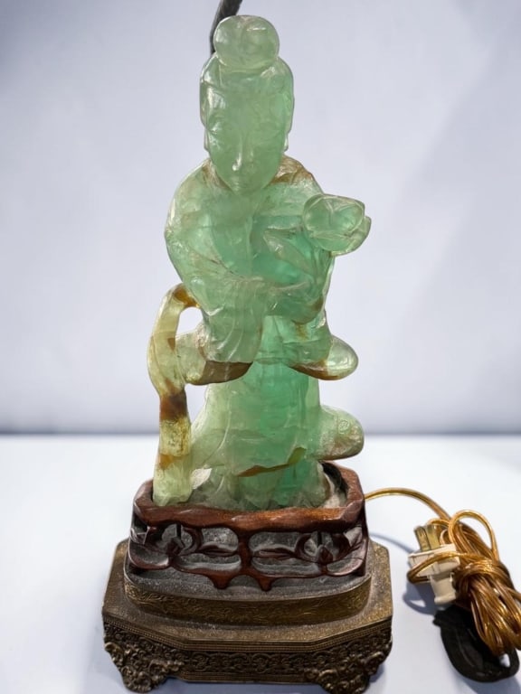 Chinese Carved Green Hardstone Guanyin Lamp Base: Chinese Carved Green Hardstone Guanyin Lamp Base Chinese carved green hardstone figure depicting Guanyin holding a lotus blossom, rendered in translucent green stone with russet inclusions. Raised on 