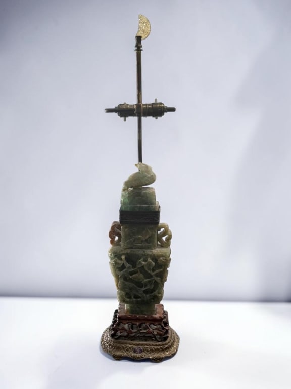 Chinese Carved Green Hardstone Vase Lamp Base: Chinese Carved Green Hardstone Vase Lamp Base Chinese carved green hardstone vase-form lamp base, featuring openwork decoration, stylized handles, and a carved bird finial. Mounted on a carved wood st