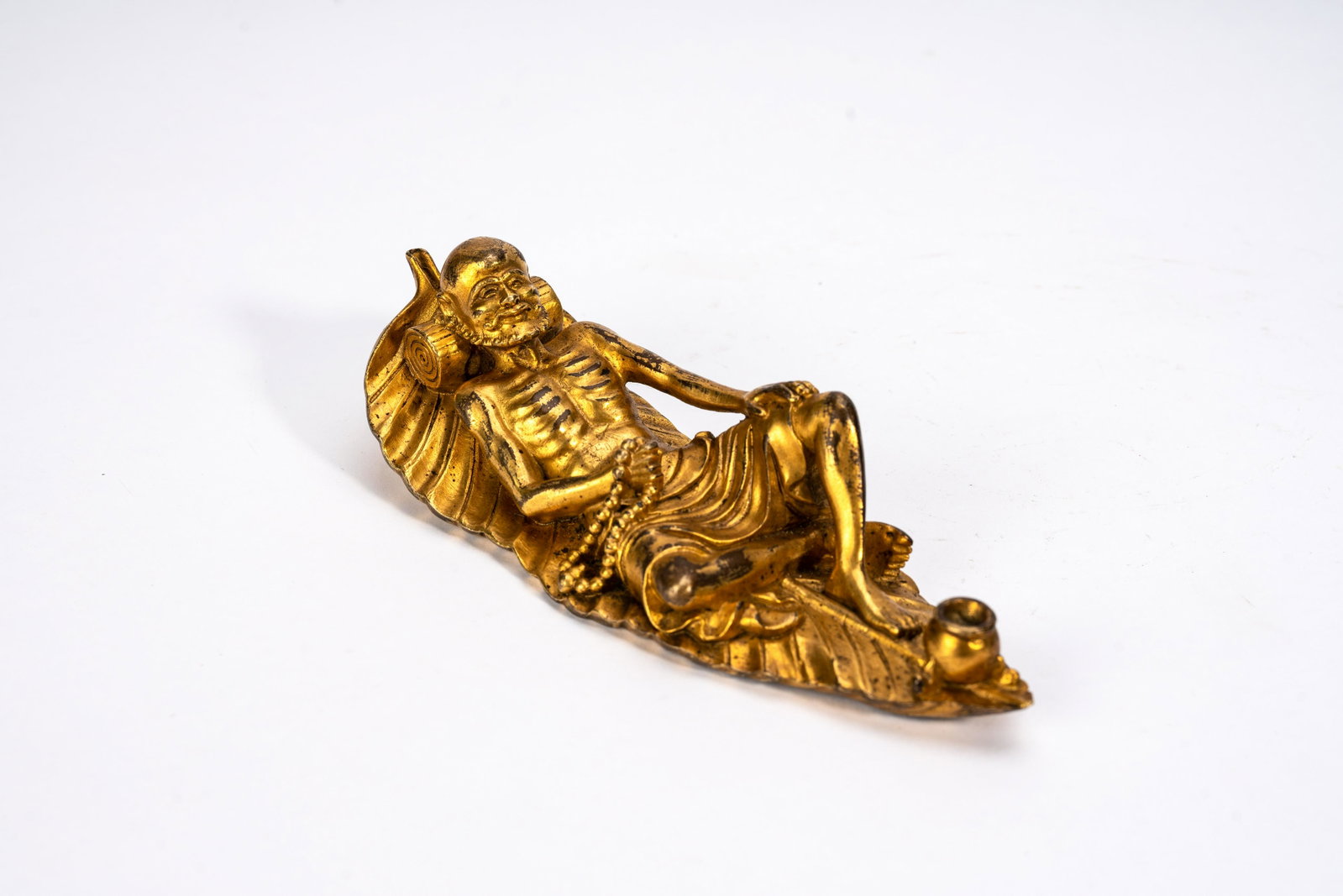Chinese Gilt Bronze Luohan Brushrest: Chinese Gilt Bronze Luohan Brushrest Chinese Gilt Bronze Luohan Brushrest, cast as a skinny arhat reclining on large leaf, overall in gilt. Qing period. 6 1/2 in (16.5 cm) From the collection of Mr. S