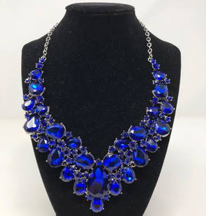 Glamorous Blue Crystal Necklace: Description: Glamorous deep blue and silver tone evening wear necklace, comprised of beautiful, faceted stones set intosilver tone metal. Manufacturers tag on link chain. Material: glass; metal. Measu