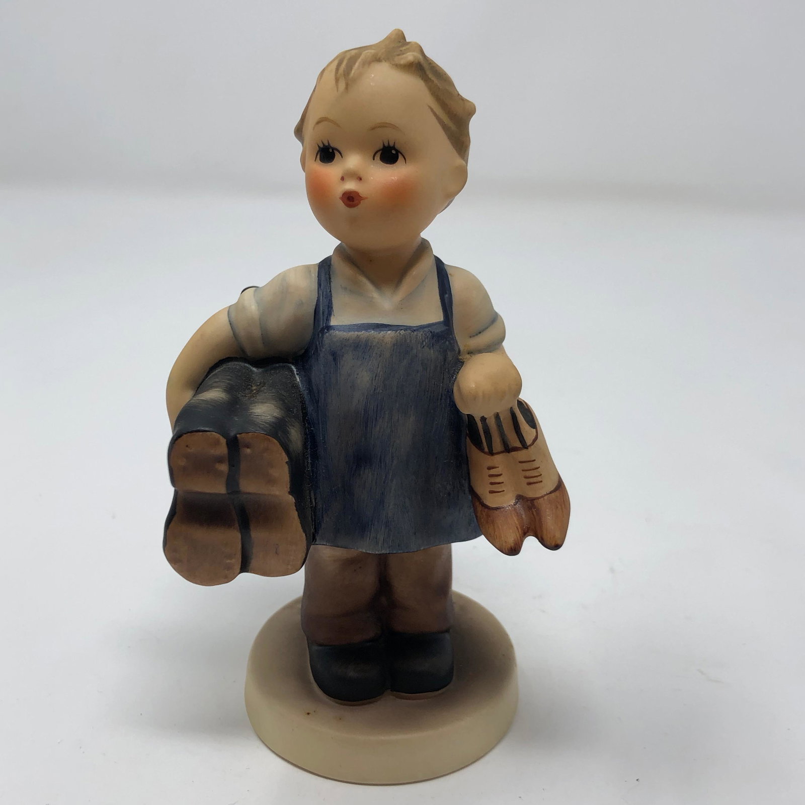 Vintage Goebel Hummel #143/0 "Boots" TMK-3: Description: Cute vintage Goebel Hummel #143/0 "Boots" TMK-3, made in W. Germany. Charming figurine depicts a small boy wearing a blue cobbler's apron and holding 2 pairs of old fashioned shoes. Signa