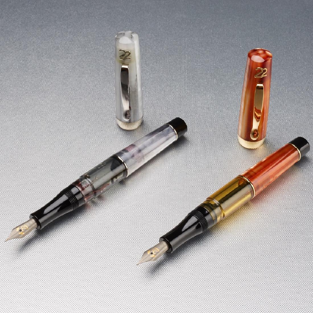 Pair Stipula Ventidue Pens: Pair of Stipula Ventidue fountain pens. One white and one orange resin, both with ink windows, both with fine titanium nibs. Numbers A2250 and A2505, respectively. Along with paper. From the collectio