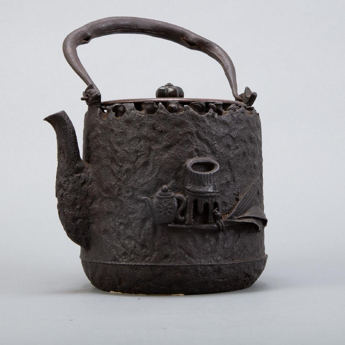 Meiji Japanese Iron Kettle Attributed to Ryubundo: Japanese tetsubin iron kettle with an iron lid attributed to Ryubundo. Both sides have designs in high relief--one of flowers and the other of a tea scene. The kettle has a signature along the undersi
