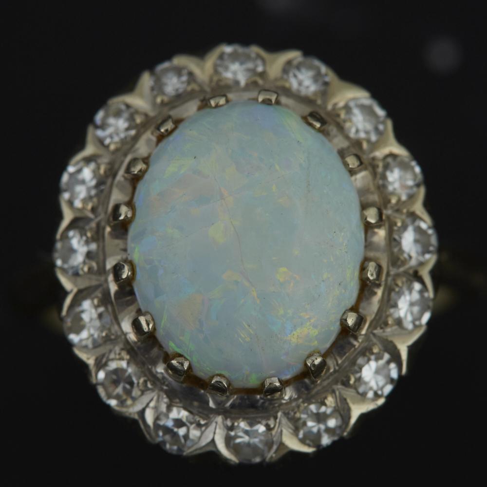 Opal and Diamond Ring 14 K White Gold: Halo-set opal ring with an oval-shaped opal and sixteen diamonds with a 14 K gold band. Band is marked 14K along the interior. Size 5 1/2. Dimensions: Opal measures: height: 12.23 mm x width: 10.13 mm