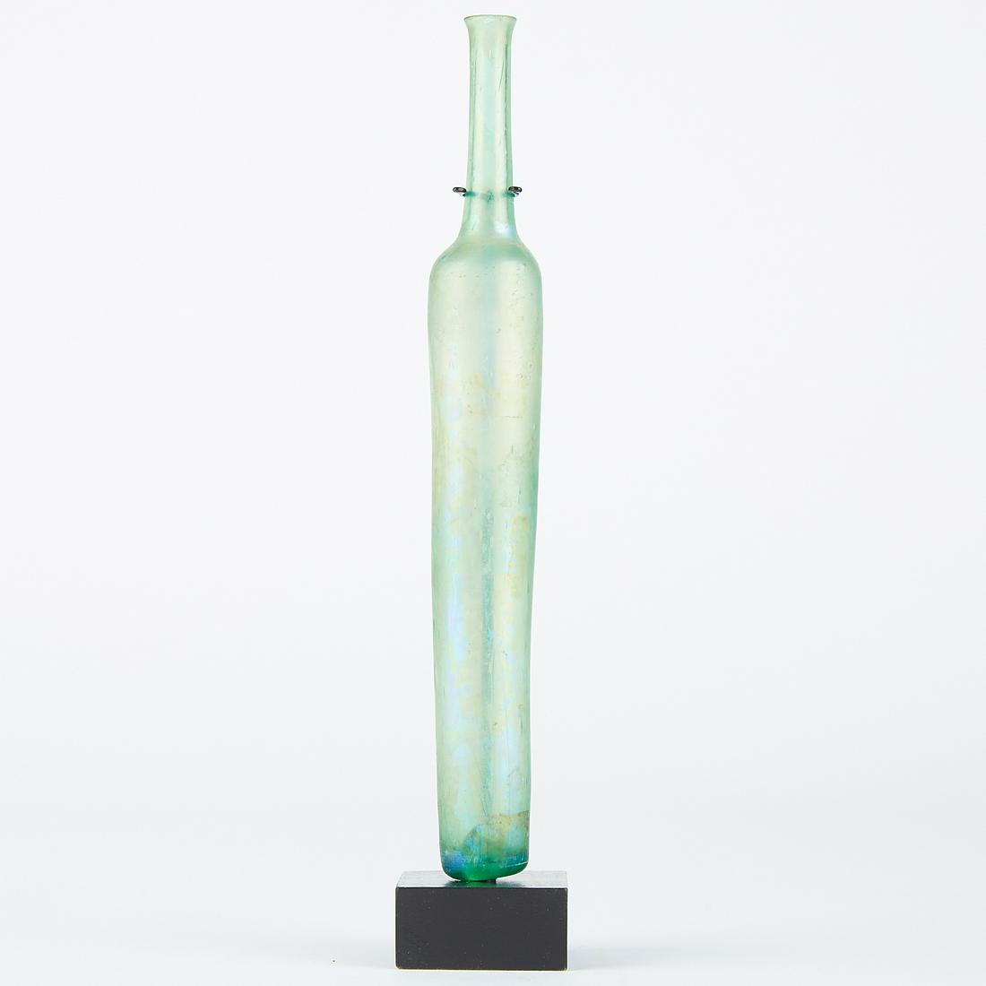 Roman Glass Unguentarium: Roman aquamarine glass unguentarium, ca. 4th c. CE. Held perfumed oils, sometimes used for embalming. Dimensions: Height: 10 1/8 in x diameter: 1 1/4 in. SKU: 02923