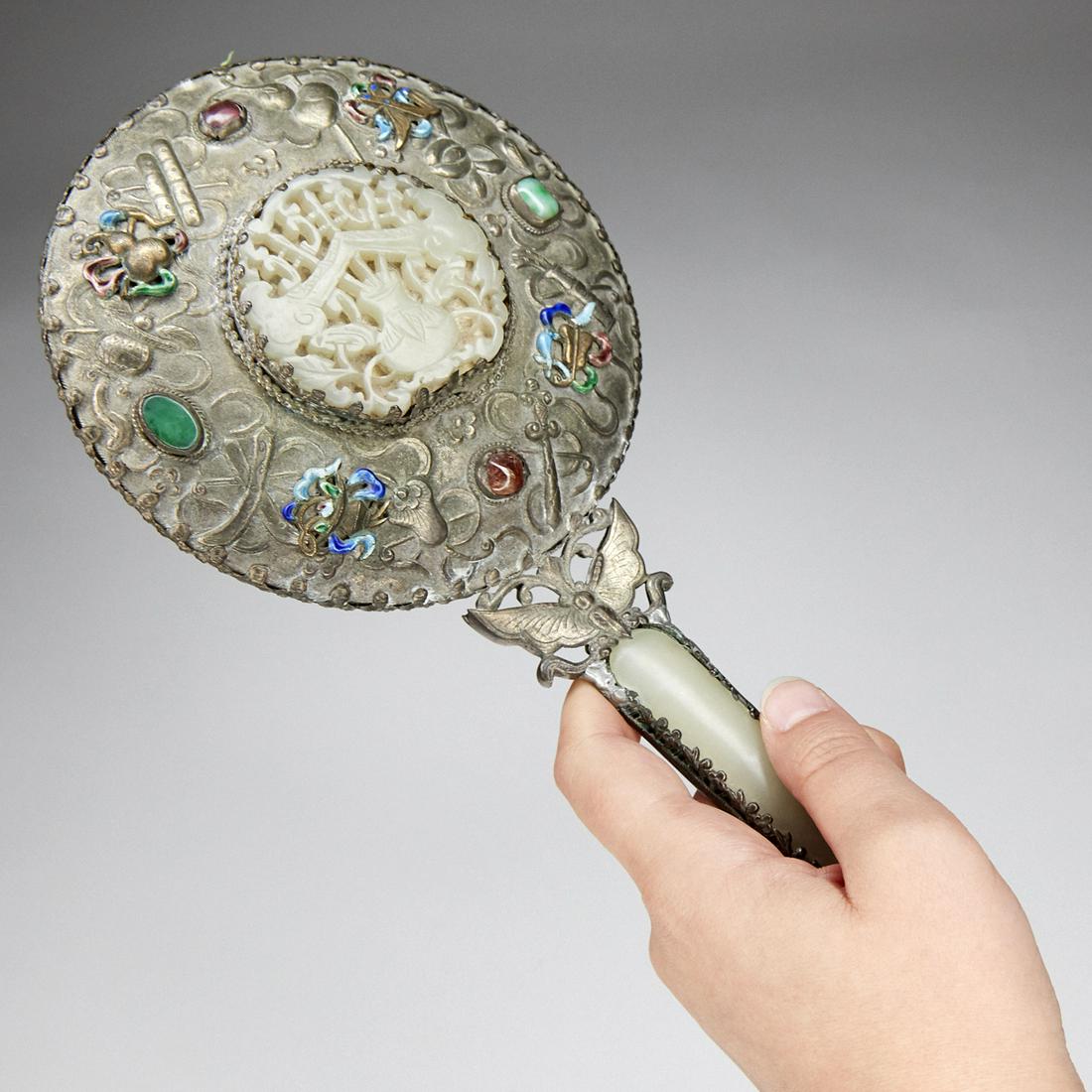 20th c. Chinese Jade Hand Mirror w/ Applied Decoration: 20th century Chinese jade and silver hand mirror decorated with enamelwork and precious stones. A lovely knotted tassel hangs from the end. Height: 11 1/2 in x width: 5 in x depth: 1 in.