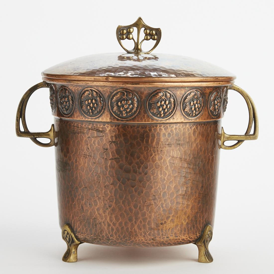 WMF German Copper & Brass Ice Bucket: WMF, Germany. Copper and brass ice bucket with decoration depicting grapes. Copper body has a hammered surface, and stands on three brass feet, with two brass handles and a brass finial on the lid. WM