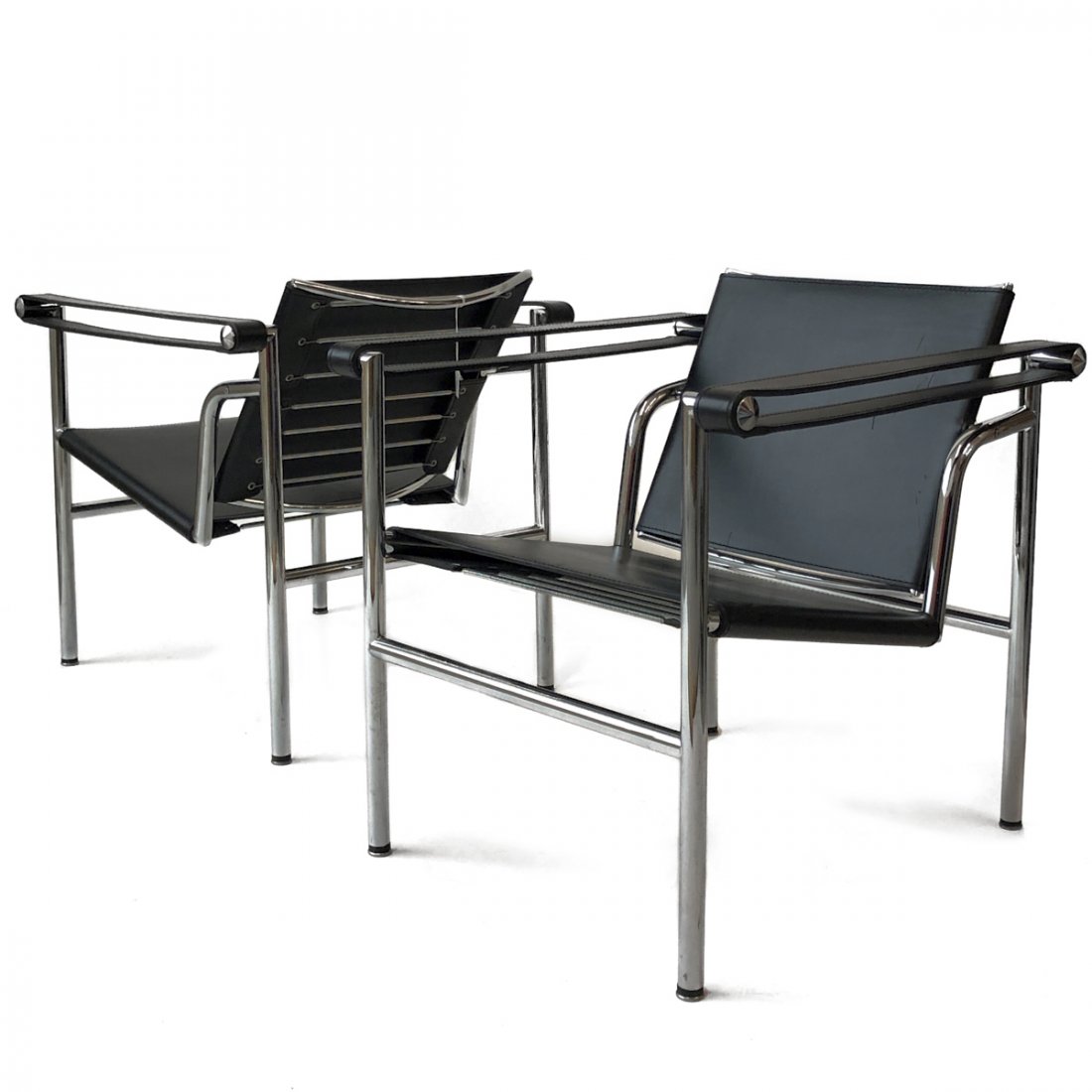 Pair of Le Corbusier Style LC1 Basculant Chairs: Pair of Room and Board Le Corbusier style LC1 Basculant chairs with a tubular chrome-plated steel frame and Italian hide black leather seat, swivel back, and armrests.Each; height: 26 in x width: 22 1