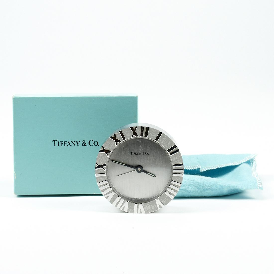 Tiffany & Co. Atlas Desk Table Clock: Tiffany & Co., New York, USA. Atlas desk or table clock in silver-tone metal with Roman numeral markers along the outer ring and brand stamp at center. Marked "Tiffany & Co. Swiss Made." and