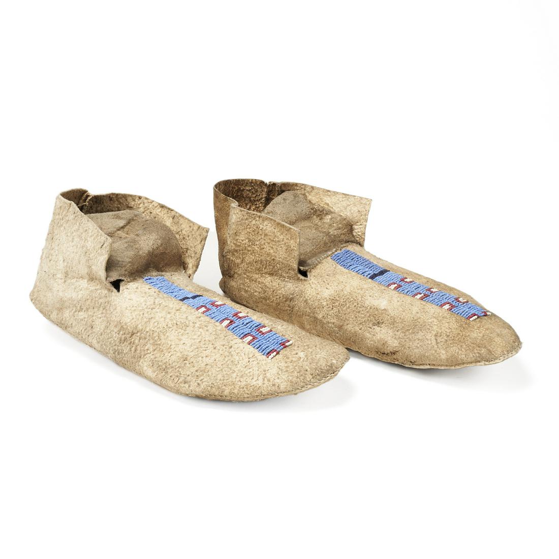 Pair of Plains Beaded Hide Moccasins Stripe: Pair of Native American Plains hide moccasins decorated with blue, red, black, and white beads in a stripe pattern along the toes, ca. 1890-1910. Each; height: 3 3/4 in x width: 4 in x depth: 10 3/4 i