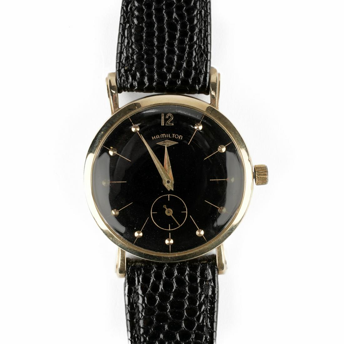 Hamilton 14K Gold Round Wristwatch: Hamilton Watch Co., Lancaster, Pennsylvania, USA. 14K yellow gold circular black enameled wristwatch, marked "Hamilton" along the dial, with 18 mm black leather band. Marked "14K Hamilt