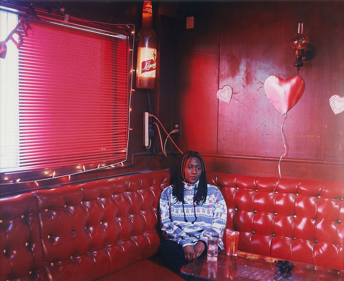 Alec Soth "Kym" Large C-print Photograph: Alec Soth (American, b. 1969). Large chromogenic print photograph titled "Kym" depicting a woman seated in a red restaurant booth lit dramatically by the sun streaming through the drawn red