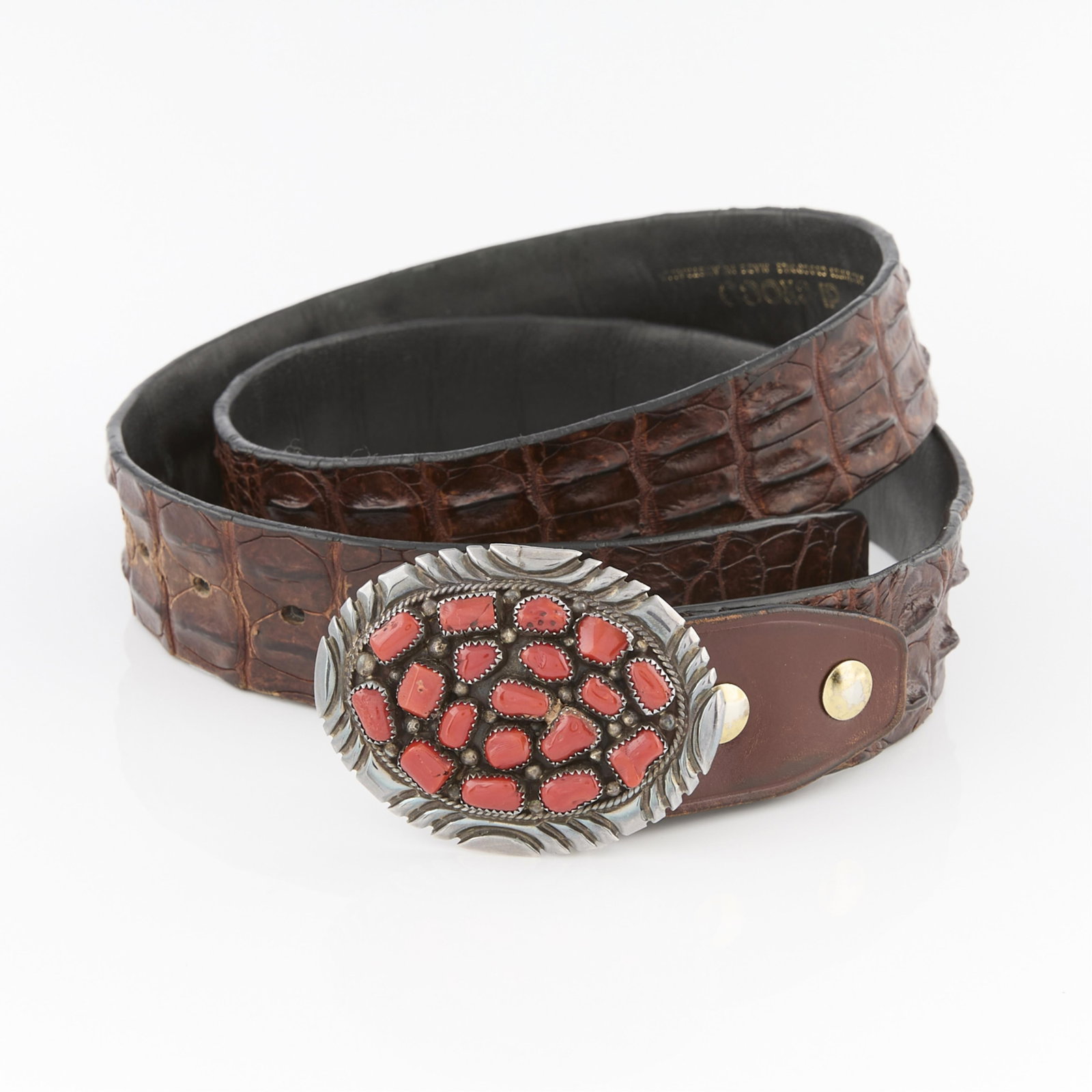 Southwest Style Belt: One oval form belt buckle set with 18 red hardstones in a border with incised semicircles. Marked E. Castil (indistinct). On a brown leather belt marked salt water crocodile made in Australia. (Buckle