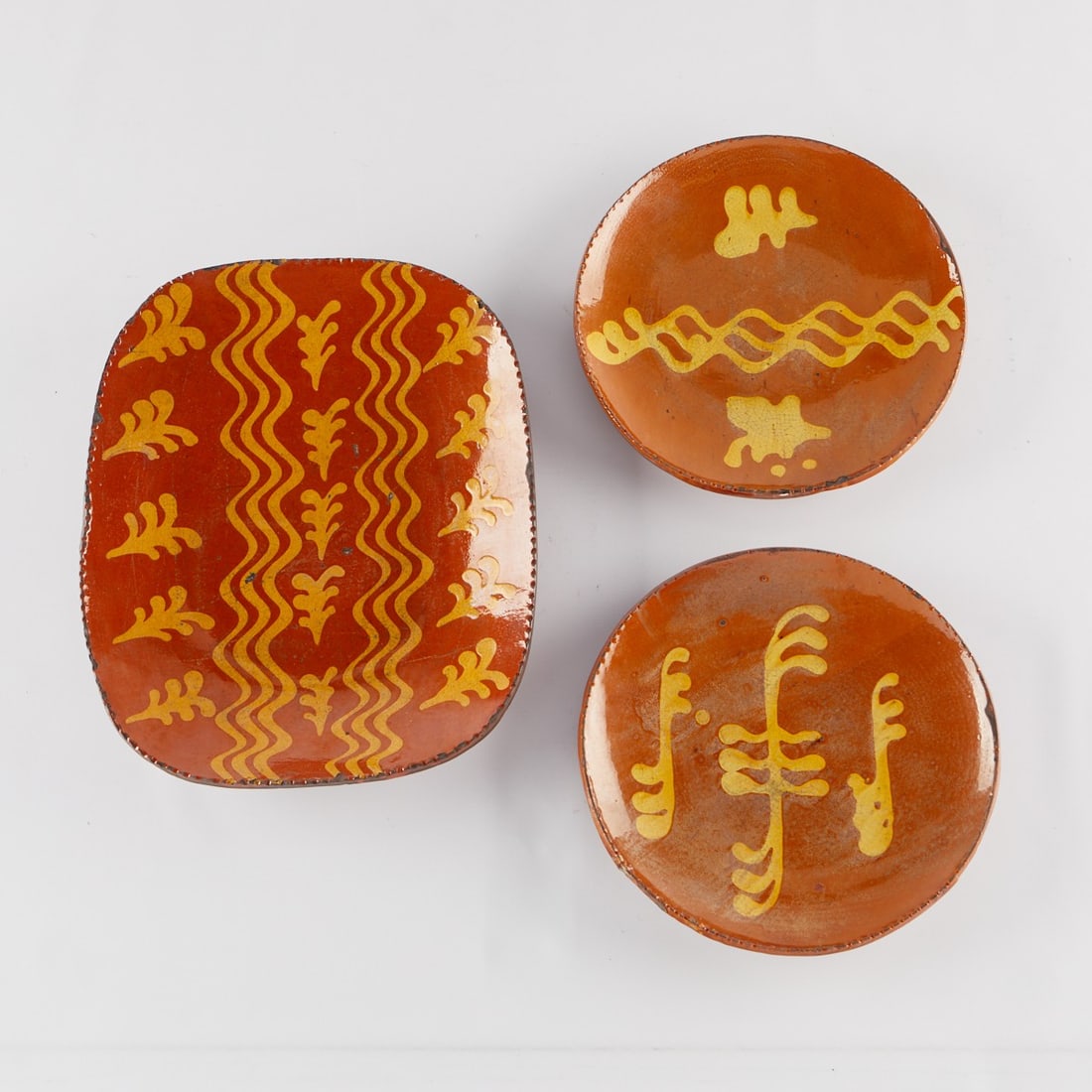 3 Modern Redware Chargers Shooner & Woods: Group of three redware slip decorated stoneware ceramic pottery chargers. The two round chargers each with an incised signature along the underside by Christopher Woods (American, 20th c.), dated 1996
