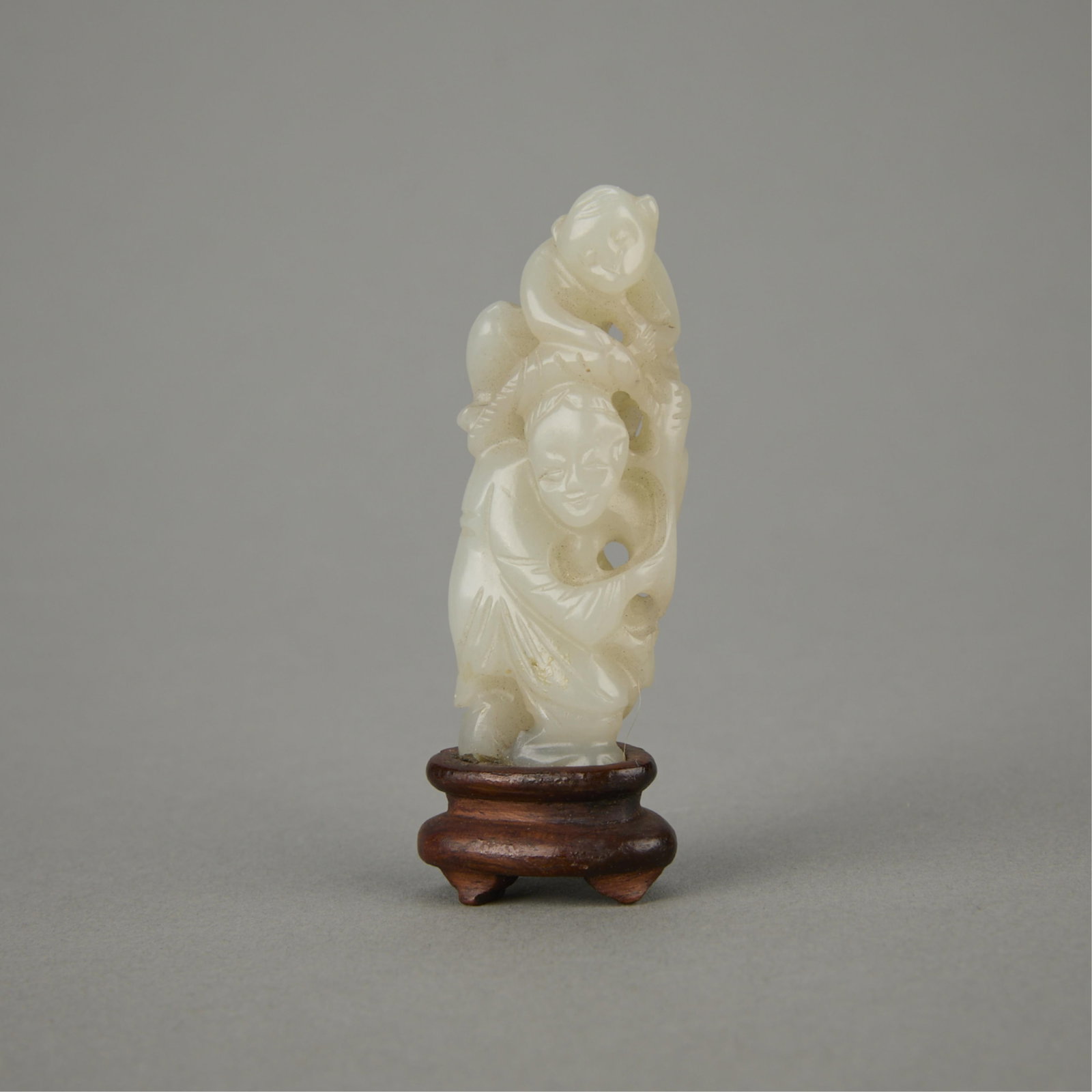 Chinese Carved Jade Boy with Monkey Figure: Chinese carved jade depicting a young boy surmounted by a monkey. The figures are of a pale coloration. Affixed to a custom carved lacquered wood stand. (Incl. stand) height: 2 1/2 in x width: 3/4 in 