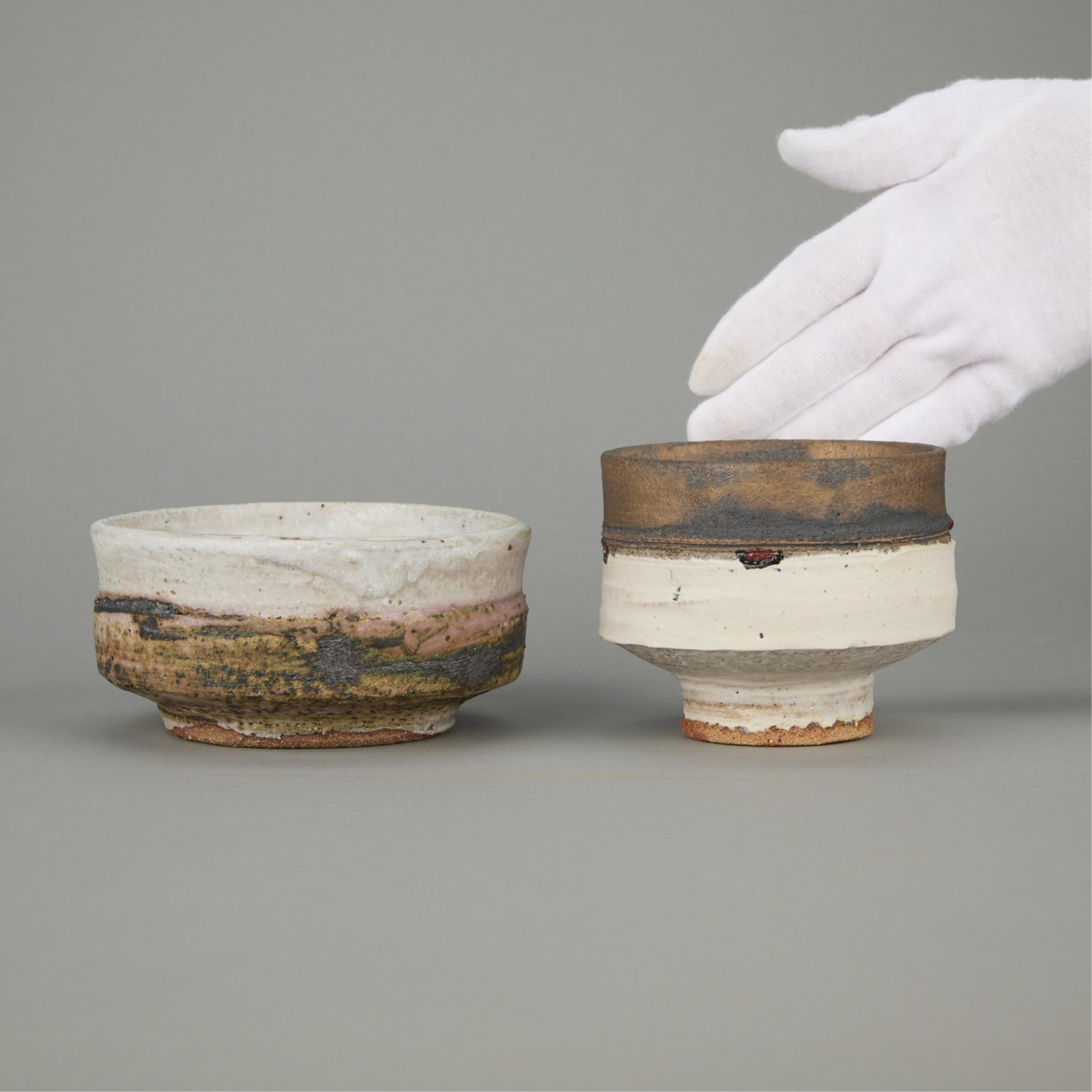 2 Robin Welch Studio Pottery Ceramic Vessels: Robin Welch (British, 1936- 2019). Group of two studio ceramic chawan (tea bowls) or cup vessels, 21st century. Stoneware with layered glazes. The taller vessel has a dolomitic matte glaze along the l