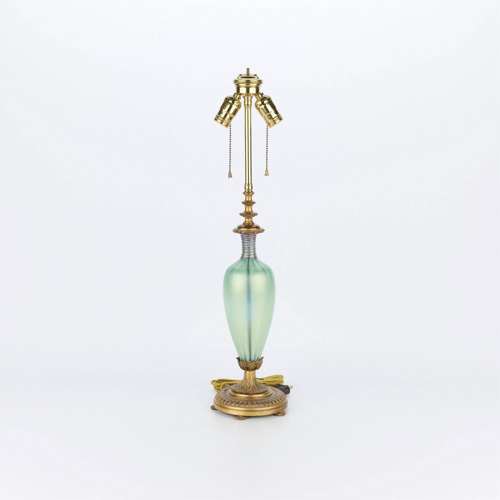 Steuben Art Deco Jade Glass Lamp ca. 1920s: Steuben, United States. Art deco oriental jade-green glass lamp surmounted atop a gilt bronze base with foliate and crest motifs in relief, ca. 1920s. There are threads of ruby glass revolving around 