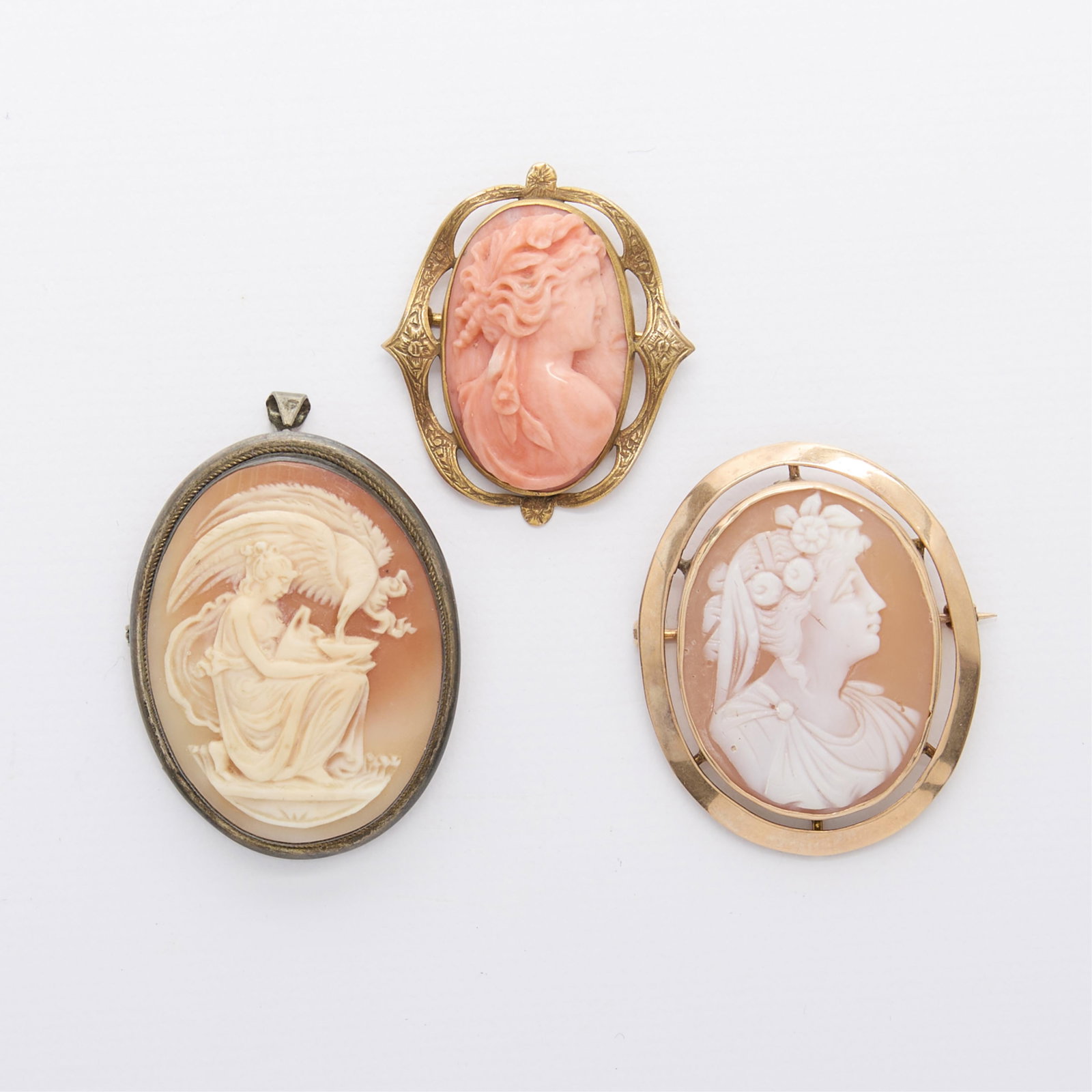 Group 3 Gold & Other Cameos: Group of three cameos including: One shell cameo depicting Hebe the cup bearer of Zeus, set in an 800 silver frame with locking c clasp closure and hidden bale. Marked 800 along the frame. One pink co