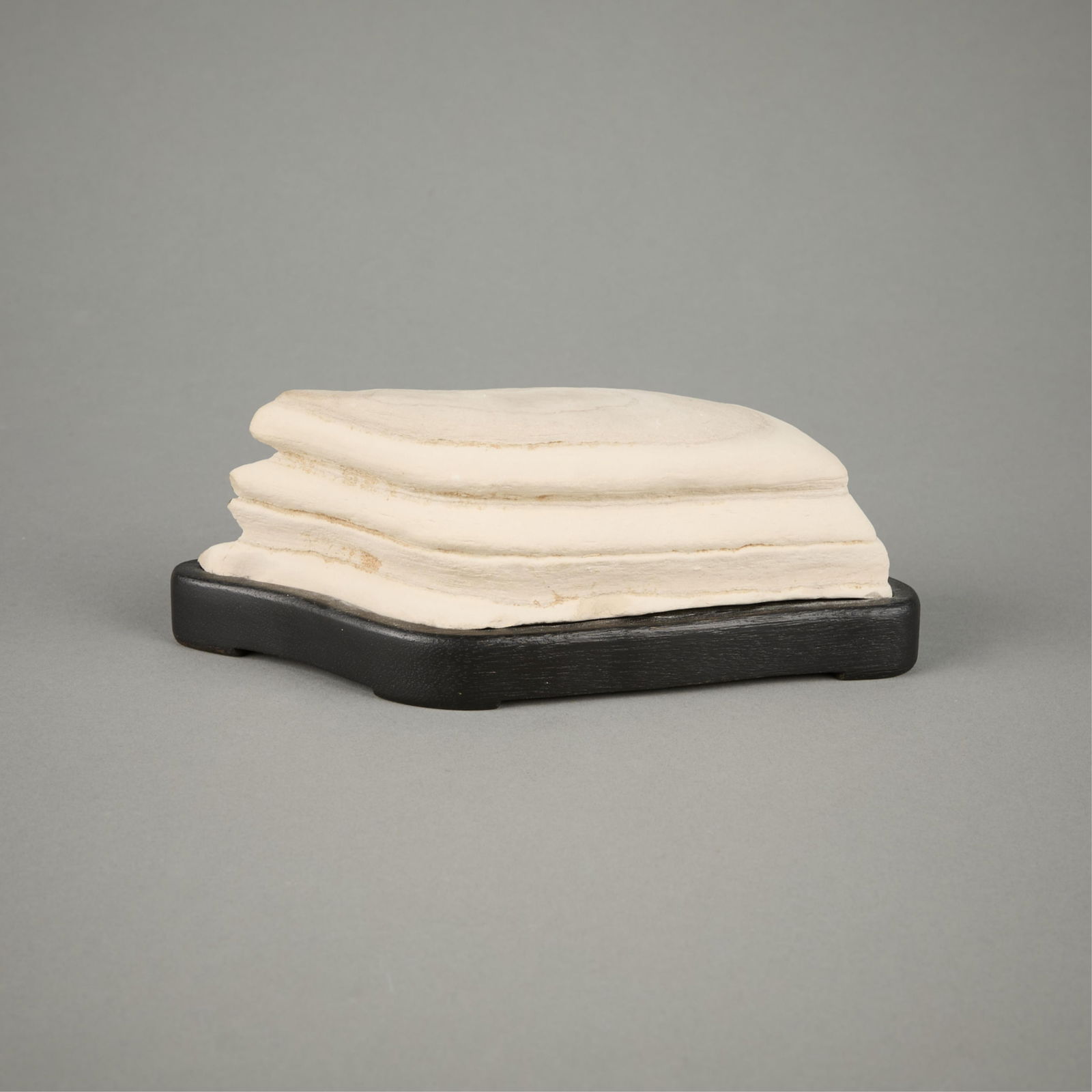 Chinese White Gongshi Scholar's Rock: Chinese gongshi scholar's rock of a rounded rhomboid form. The rock is of a matte cream white hue with layered curves and crevices throughout. Possibly taihu stone. With a custom carved lacquered wood