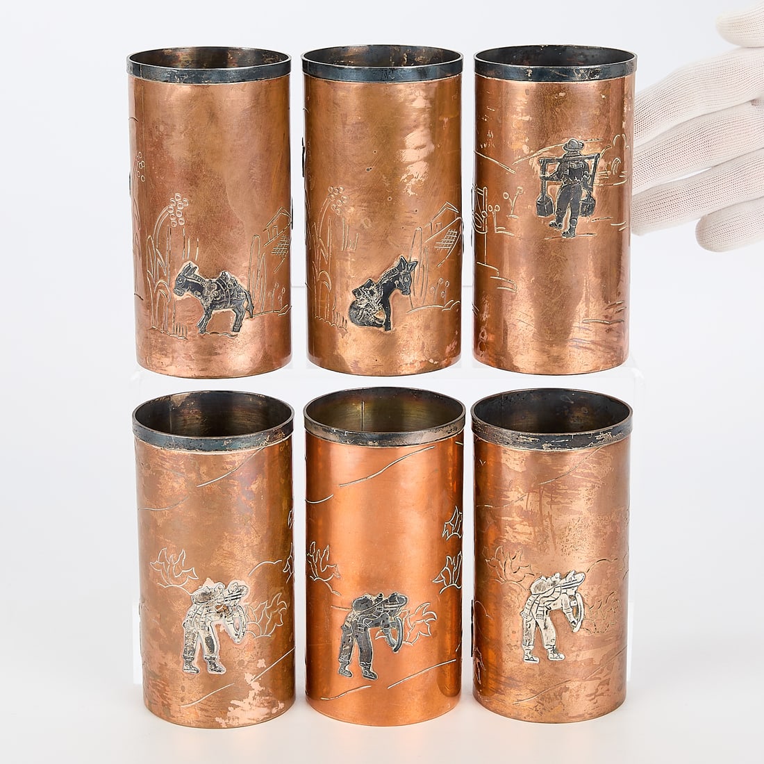Set 6 Taxco Copper & Silver Cups: Taxco, Mexico. Set of six copper tumbler cups with silver inlay depicting figures and burros. Stamped mark along the underside.(Each) height: 5 1/4 in x diameter: 2 3/4 in.