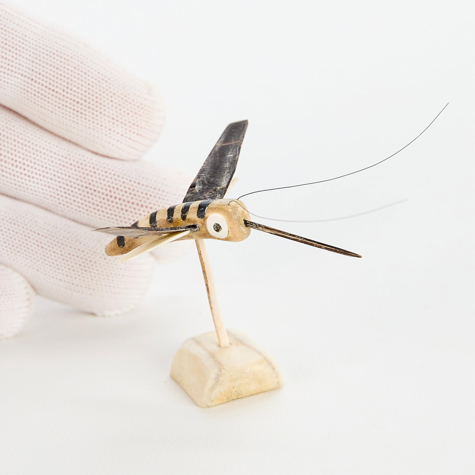 Robert Kuptana Mosquito: Robert Kuptana (Inuit (Paulatuk), 20th c). An antler, baleen and whisker sculpture of a mosquito. Mounted on a pole and set into a base. Mosquito can be removed from pole and stand. Marked in syllabic