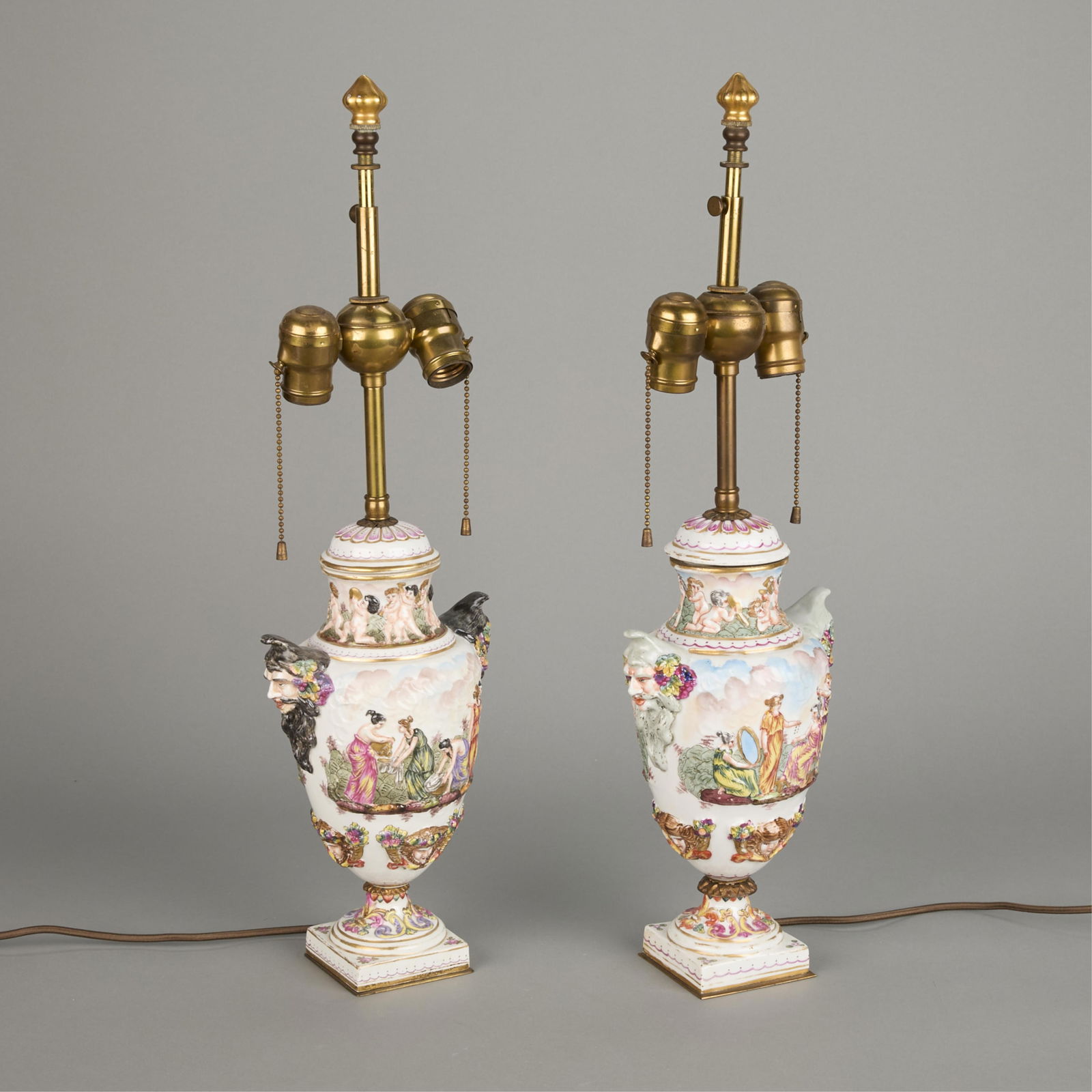 Pair Capodimonte Porcelain Urn Lamps: Capodimonte, Italy. Pair of porcelain urns or vases mounted as lamps. Hand-painted with gilt and relief decoration of neoclassical scenes.Each, Height: 22 1/2 in x width: 7 in x diameter: 5 in.