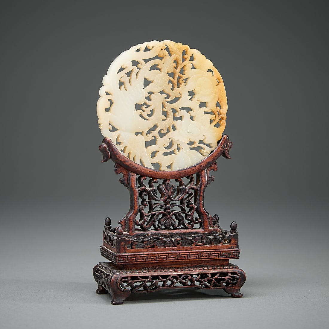 Chinese Pierced Lotus & Phoenix Jade Plaque: Chinese pierced and carved jade plaque depicting blooming lotus flowers and a phoenix. With intricately pierced and carved wooden stand. (Plaque) Diameter: 3 in. Weight: 52.44 g.