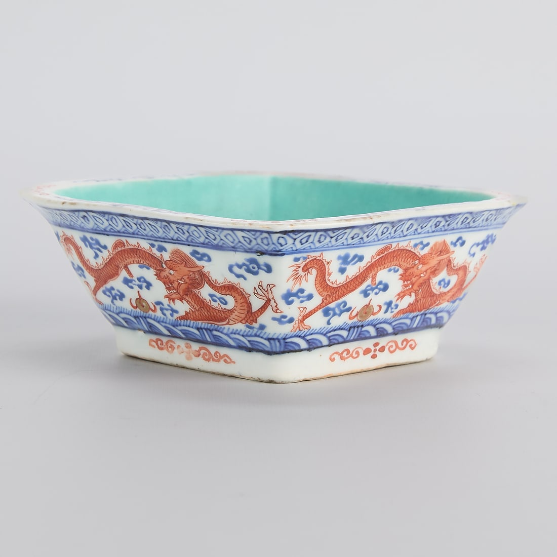 Chinese Tongzhi Porcelain Square Dragon Bowl: Chinese Qing dynasty porcelain bowl depicting iron red enameled dragons chasing flaming pearls, bordered by bands of cobalt blue geometric motifs, Tongzhi period, ca. 1862-1874. Of tapered square form