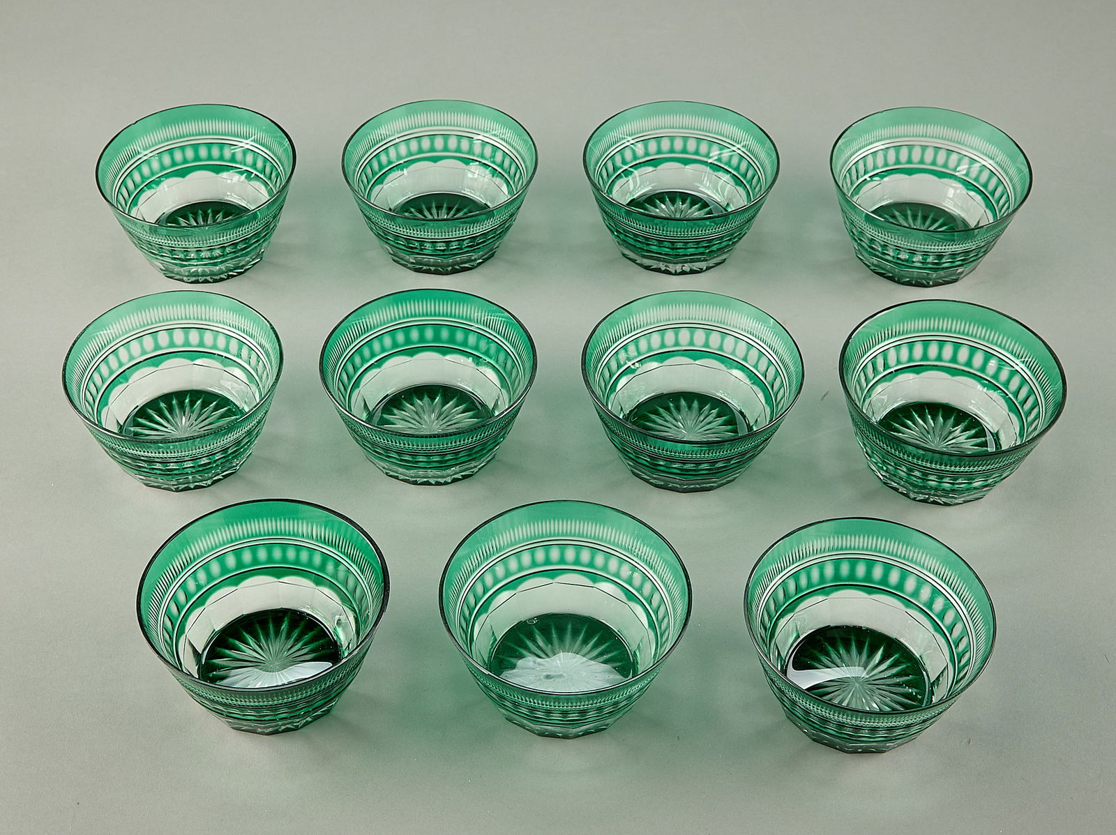 11 Emerald Green Cut Glass Crystal Bowls: Group of eleven cut glass crystal bowls in emerald green. Each depicting geometric motifs. (Each) height: 2 1/2 in x diameter: 4 3/4 in.