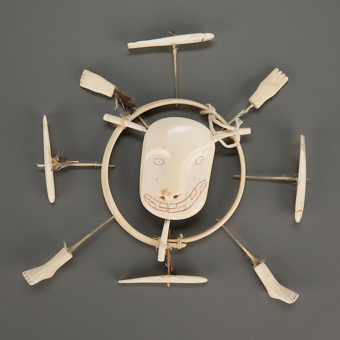 Andrew Noatak Carved Spirit Wheel Mask ca. 1940: Andrew Noatak (Yupik, 1900-1990). Carved organic material spirit wheel or mask featuring central face with incised details and pigment, ca. 1940. With hand, feet, and fish forms radiating from various