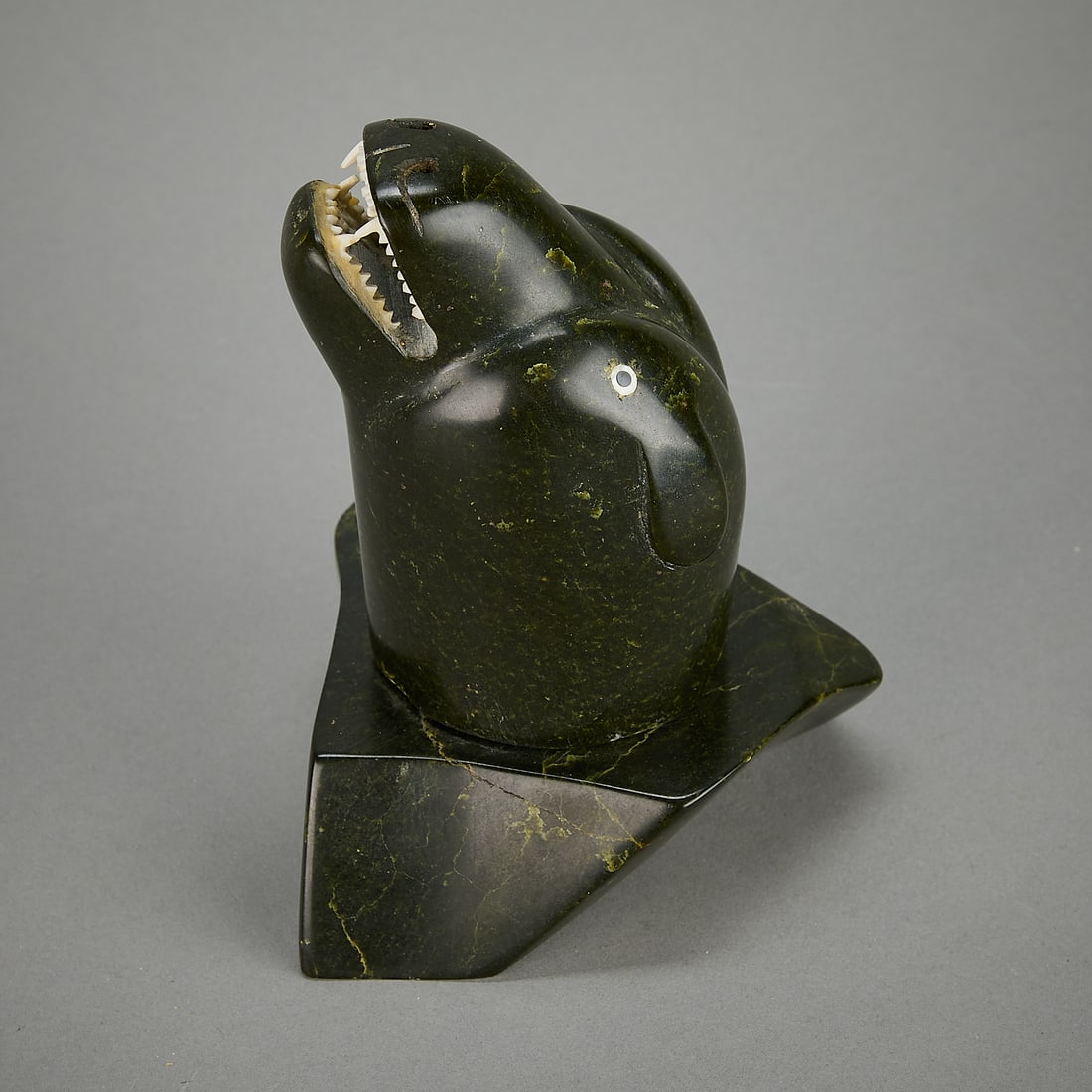 Nuveeya Ipellie Carved Stone Mammal Figure: Nuveeya Ipellie (Inuit (Frobisher Bay - Iqaluit), 1920-2010). Carved soap stone figure depicting a mammal bearing its teeth, ca. 1973. With inlaid eyes and carved organic material teeth.Provenance: He