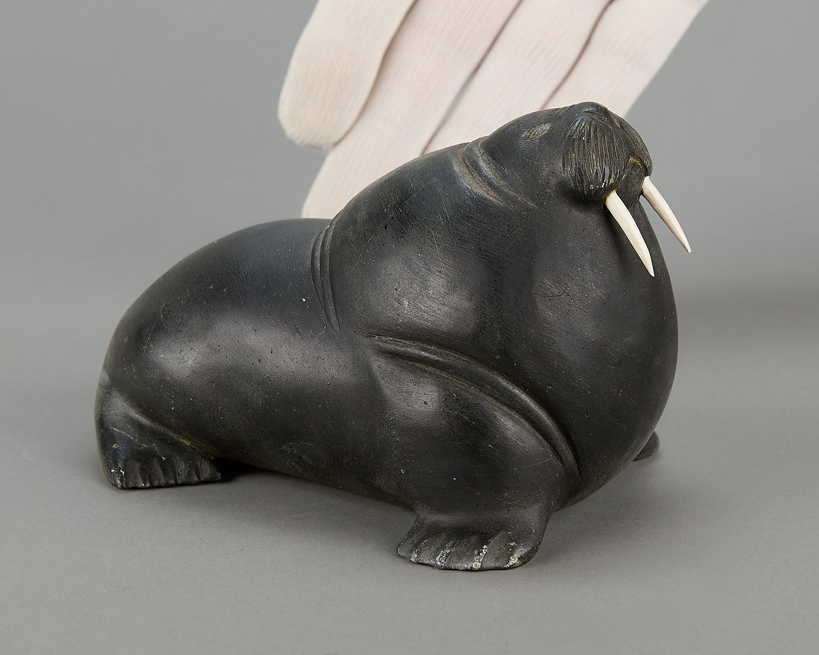 Moses Echalook Carved Mammal Sculpture: Moses Echalook (Inuit (Inukjuak - Port Harrison), b. 1931). Carved stone mammal of ample and rotund form with incised details. Signed in syllabics along the bottom with disc number and other labels.Pr