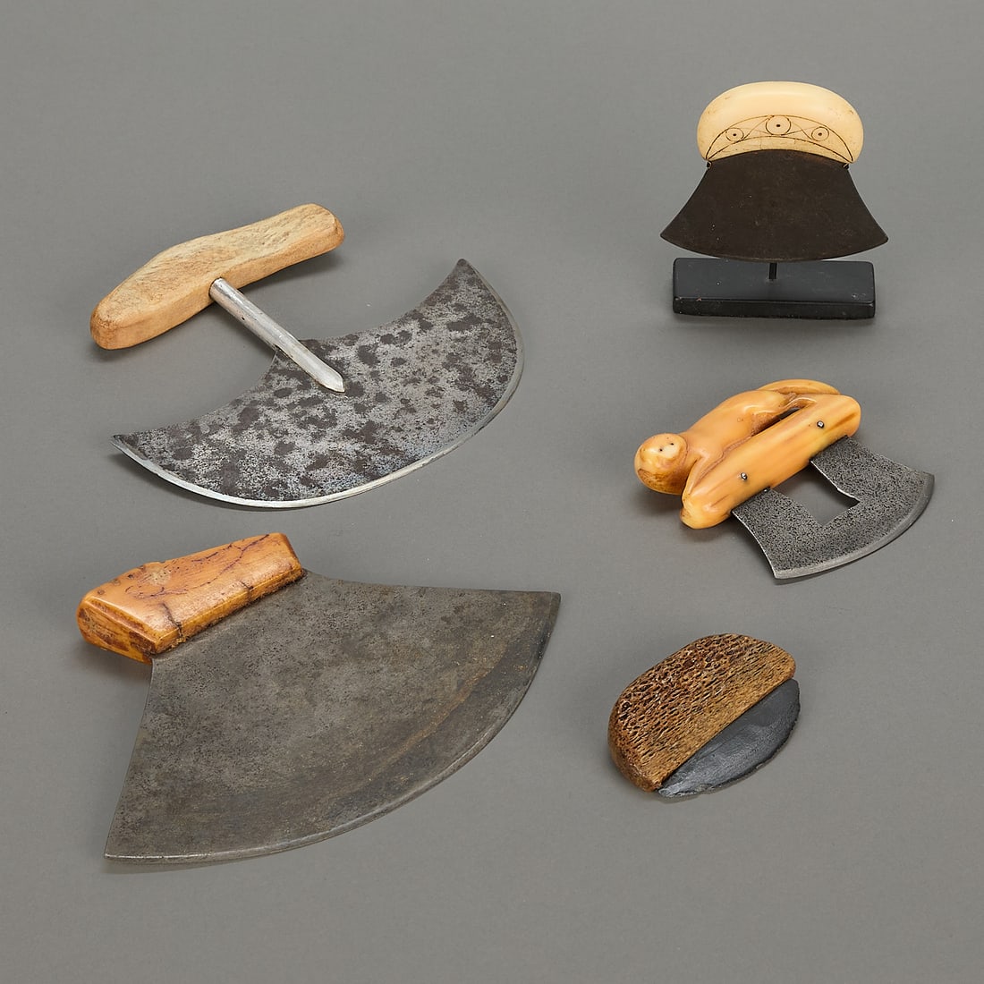 5 Inuit Ulu Knives: Group of five ulus including: One small ulu with carved organic material handle with incised circle and dot design and metal blade, on a fitted stand. One older, small ulu with organic material
