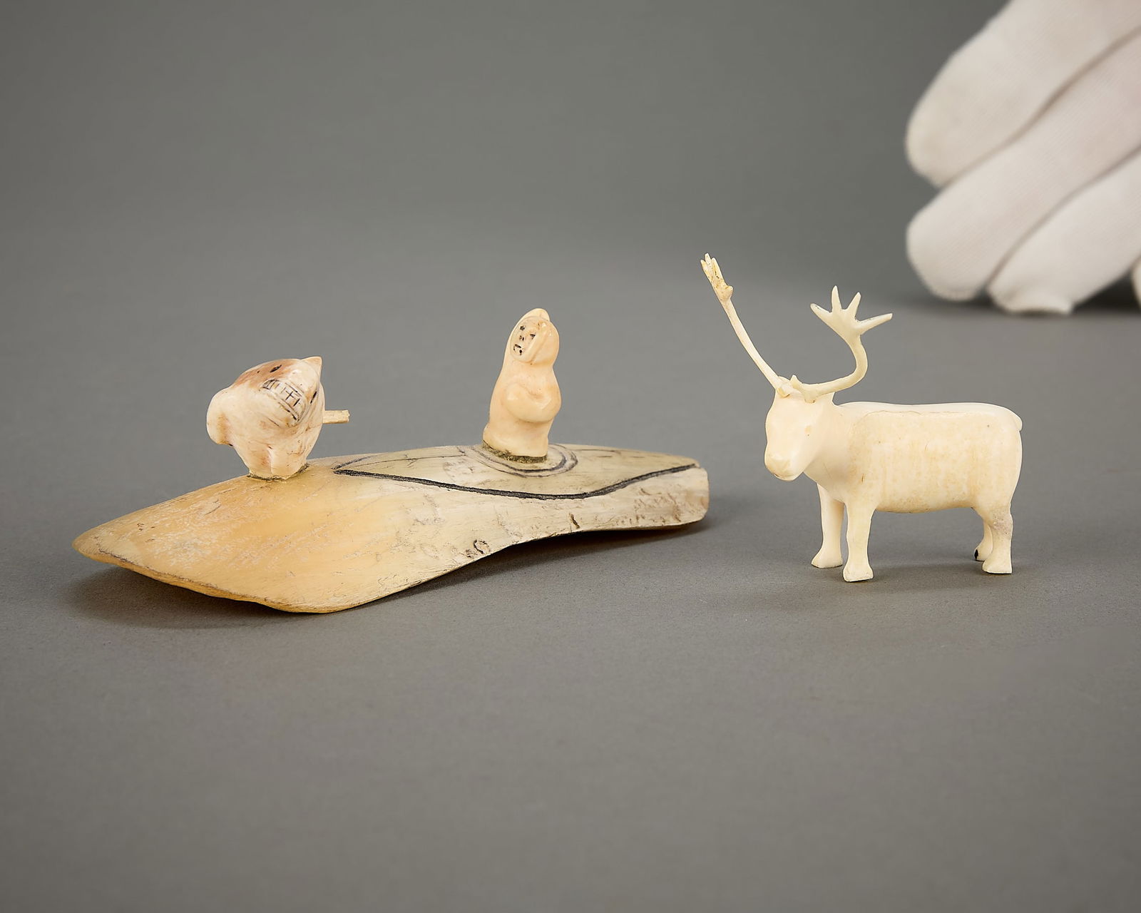 2 Inuit Carvings Incl. Tungilik: Group of two Inuit carvings. Including: Mark Tungilik (Inuit (Repulse Bay - Naujaat), 1913-1986). Carved organic material carving depicting a caribou. With incised syllabics along the underside. One c