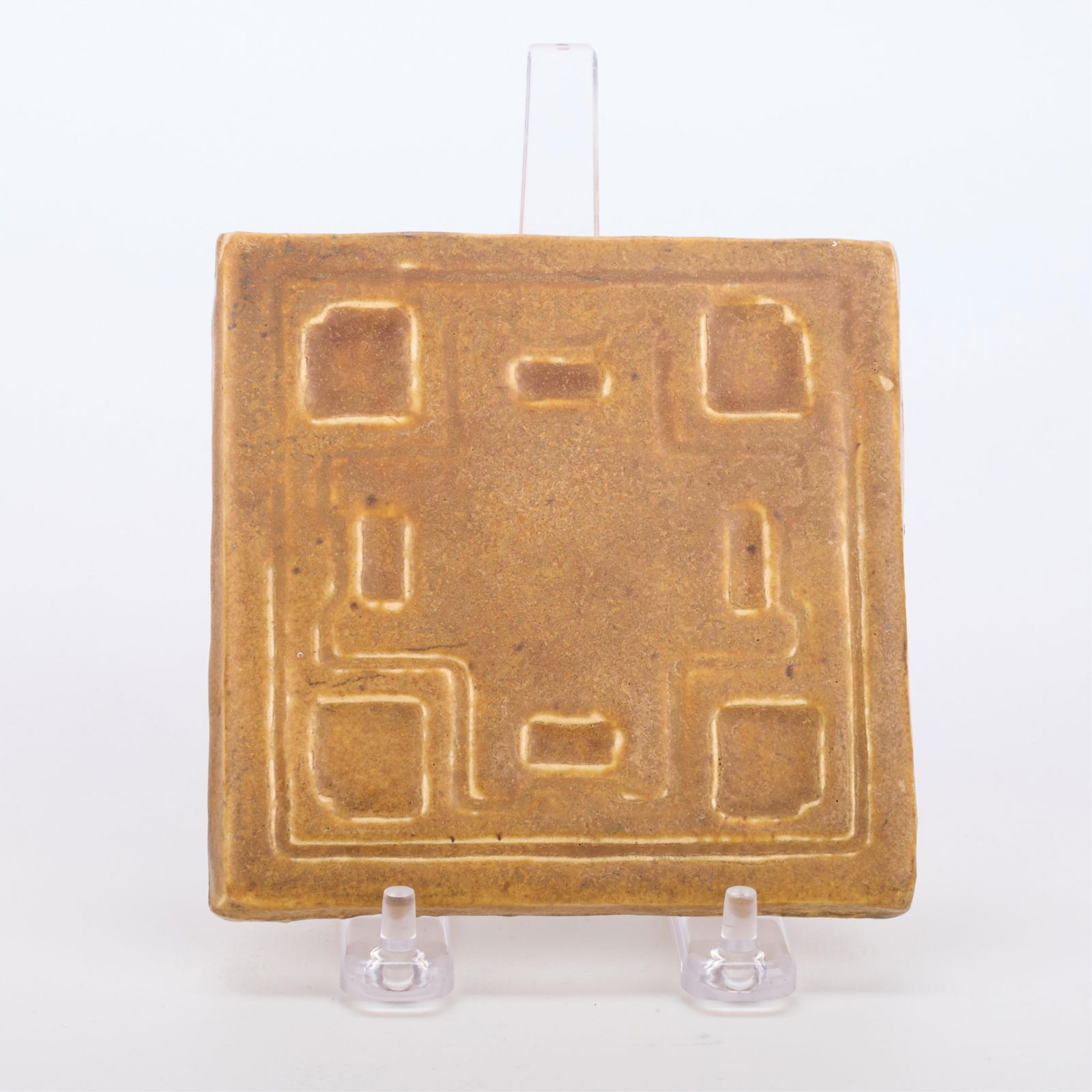 Arts & Craft Decorative Tan Pottery Tile: Arts & Crafts architectural ceramic tile or decorative coaster. Depicting geometric motifs executed in a tan brown glaze. Incised initials "B.M.C" along the underside.Height: 4 3/4 in x width: 4 3/4 i