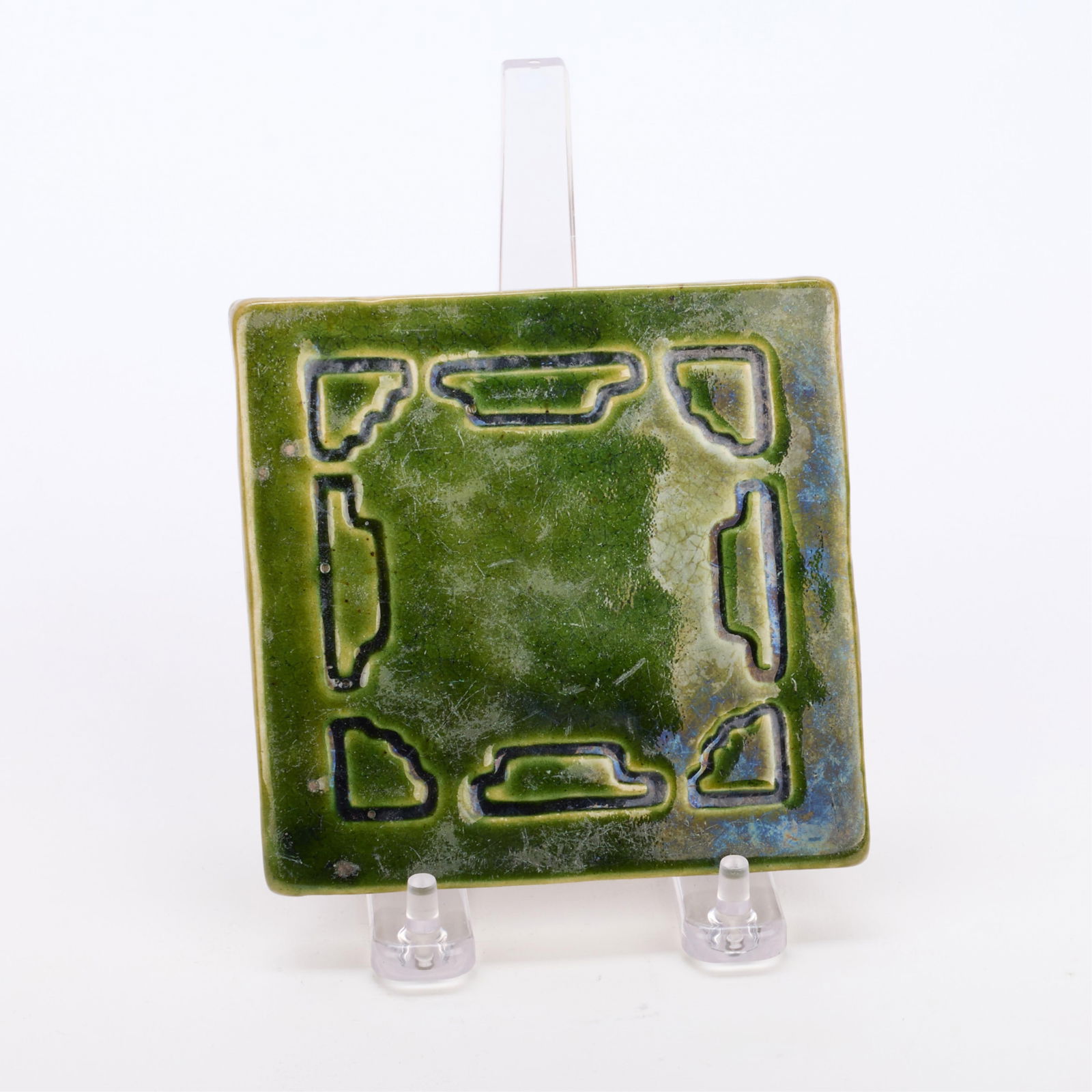 Arts & Crafts Geometric Green Pottery Tile: Arts & Crafts architectural ceramic tile or decorative coaster. Depicting geometric motifs executed in an earthy green glaze. Initialed "B.M.C" along the underside.Height: 4 1/4 in x width: 4 1/2 in x