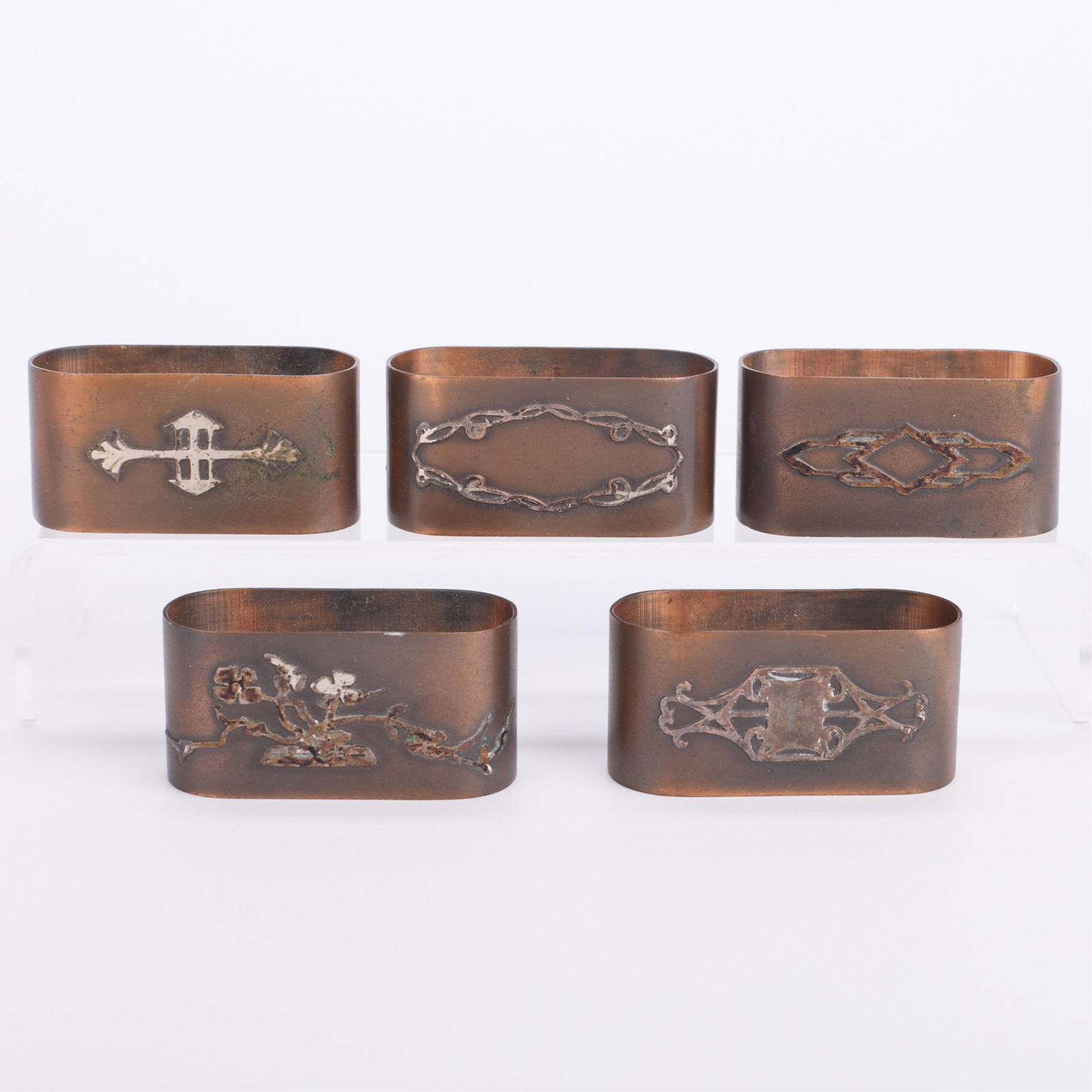 5 Attr. Heintz Arts & Crafts Bronze Napkin Rings: Attributed to Heintz Art Metal Shop, New York, United States. Set of five bronze Arts & Crafts napkin rings, ca. early 20th century. Each with unique sterling silver overlay depicting Art Nouveau-styl