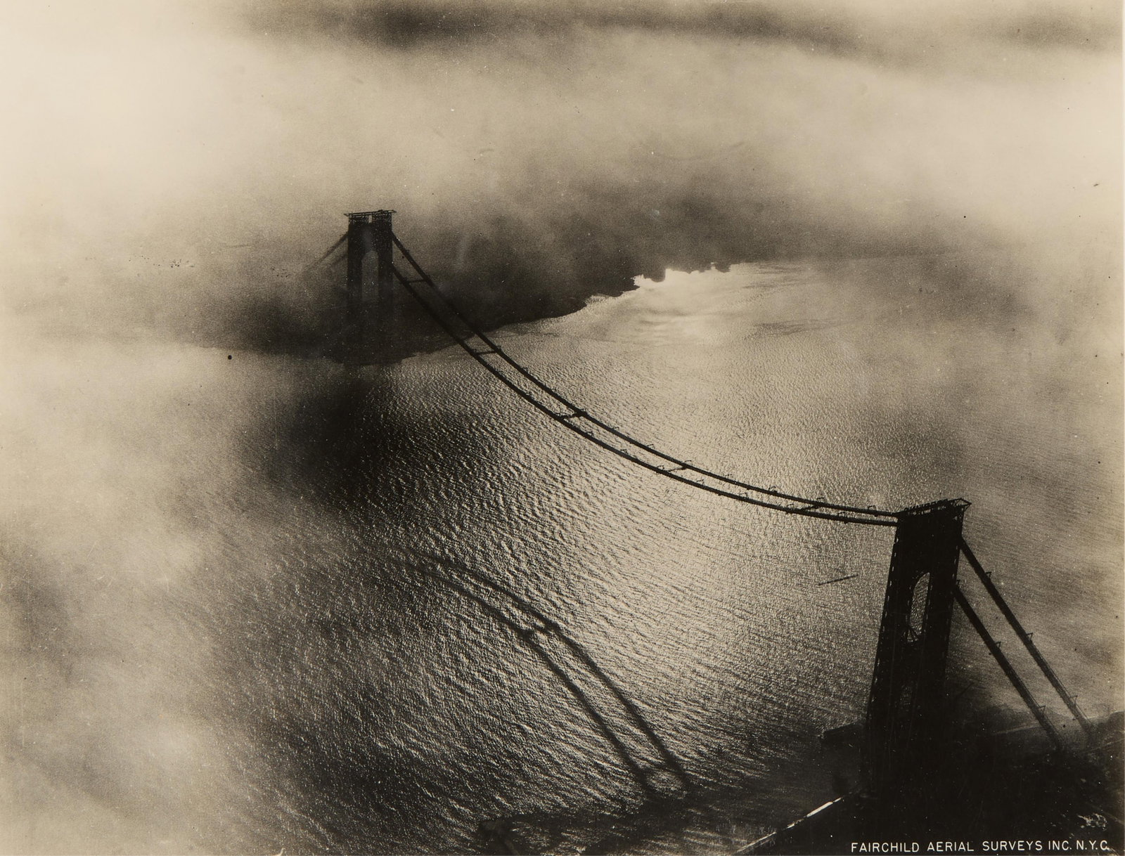 Fairchild "Hudson River Bridge" Photograph: Black and white photograph produced by Fairchild Aerial Surveys Inc., New York. Capturing an aerial view of a suspension bridge over the Hudson River shrouded in dense fog. Printed along the lower rig
