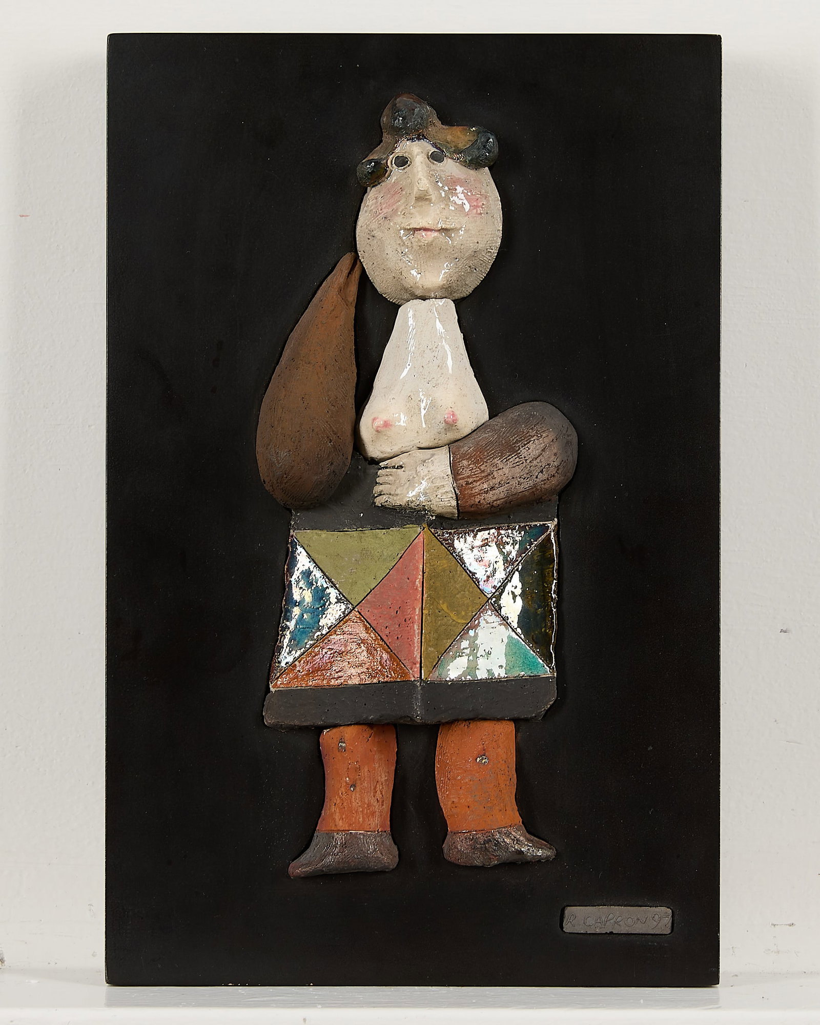 Roger Capron Woman in Box Ceramic Wall Sculpture: Roger Capron (French, 1922-2006). Ceramic wall sculpture depicting a stylized woman with exposed breasts wearing a colorful, geometric box around her waist. Embossed signature and dated 1997 along a p