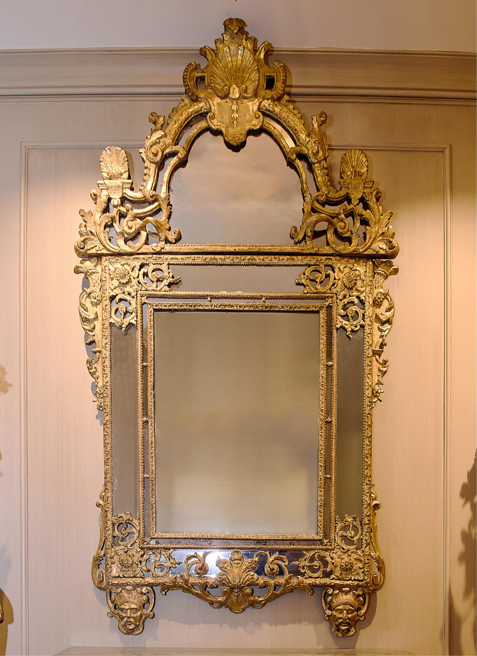 French Regence Carved Giltwood Mirror: French Regence carved giltwood overmantel mirror, 18th century. With associated cresting and later peripheral carvings. The arched cresting centered with carved shell decoration above a rectangular pl
