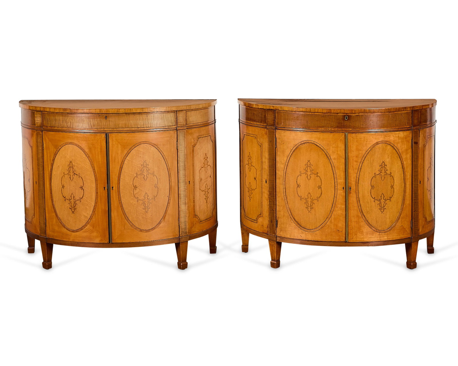 Pr George III Style Demilune Console Tables: Matched pair of George III style satinwood and mahogany demi-lune console tables. One late 19th century and the other 20th century. Each with two cupboard doors opening to reveal three drawers. On a p