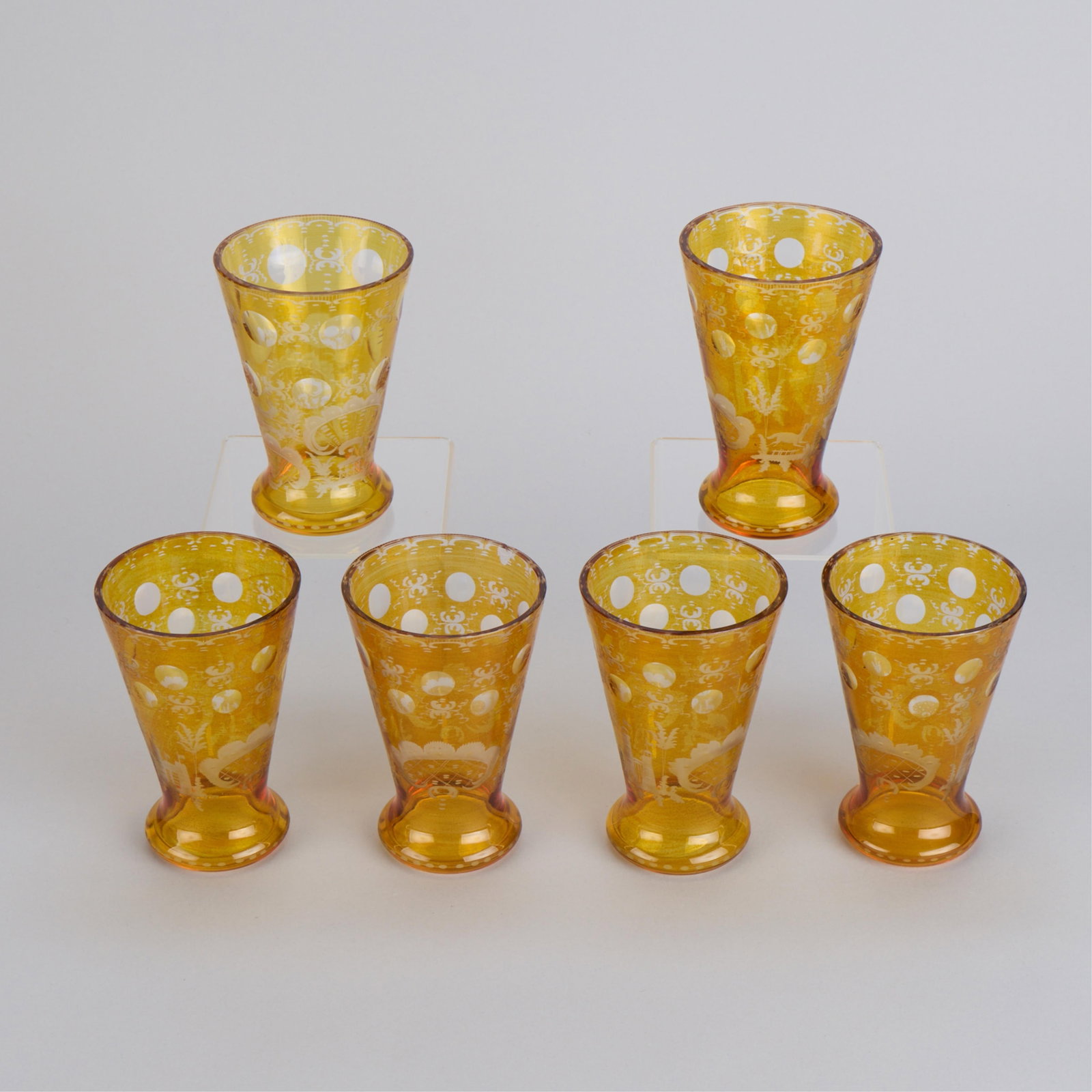6 Amber Bohemian Cut-to-Clear Glass Tumblers: Set of six Bohemian amber cut-to-clear overlay glass tumblers, early 20th century. Each depicting etched scrolling foliate motifs between cut circular facets, tapering towards the rounded bubble foot.