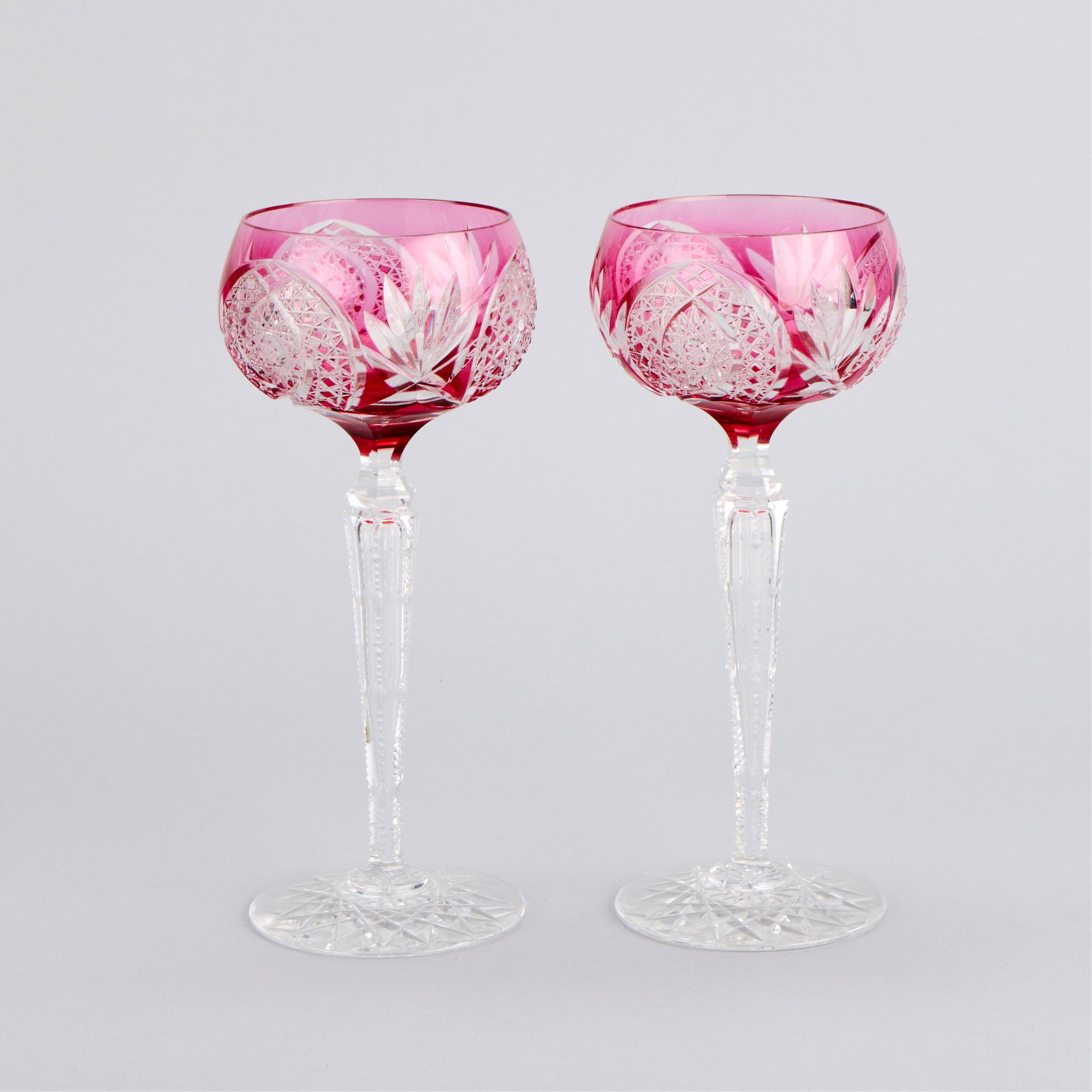 Pr Cranberry Bohemian Cut-Crystal Glass Wine Hocks: Pair of Bohemian cranberry red or pink-overlay and cut-to-clear crystal glass wine hocks or goblets, early 20th century. Each with a delicate, faceted stem resting on a star-cut foot. The bowls cut wi