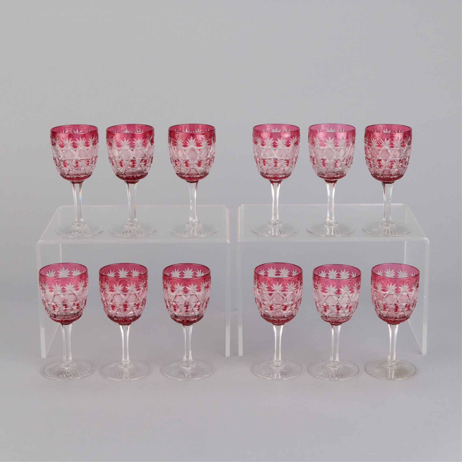 Set 12 Bohemian Cranberry Cut-to-Clear Cordials: Set of twelve Bohemian cranberry red or pink-overlay and cut-to-clear crystal cordial or liqueur stemware glasses, early 20th century. Each with a delicate, faceted stem resting on a star-cut foot. Pr
