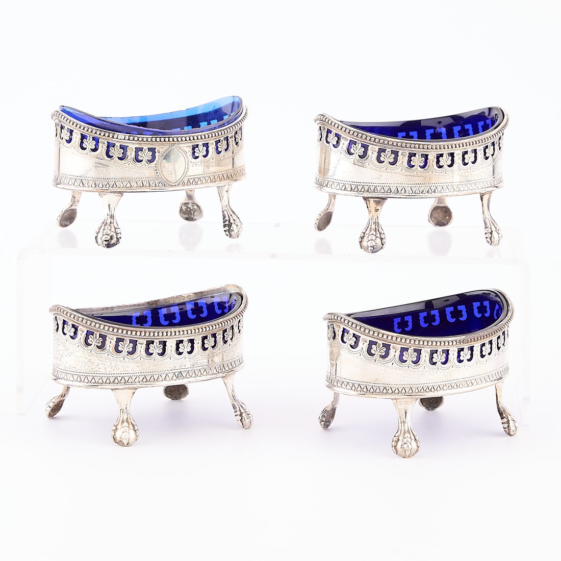 4 English Sterling & Cobalt Glass Salt Cellars: Set of four English sterling salt cellars, each on four claw feet, of oval form with decorative detailing and pierced work, each with cobalt blue glass lines. Each marked RH (potentially for Robert He