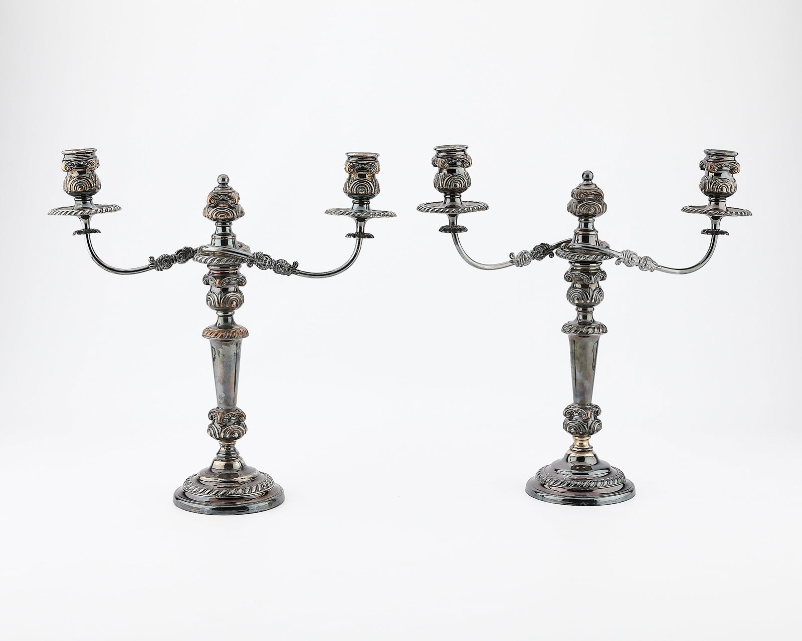 2 English Silverplate Candelabra: Pair of English silverplate two light candelabra. Weighted, with round bases and scrolling details, arms can be removed and the bases used as single candle sticks. Provenance: The Distinguished Collec