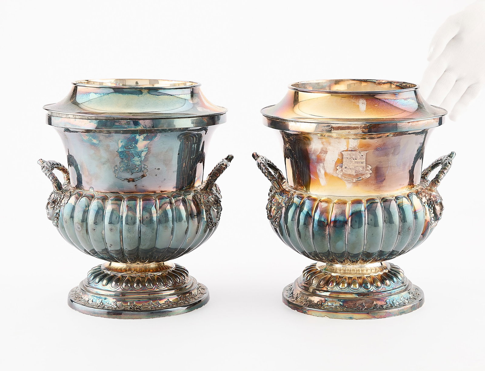 Pair of Silverplate Wine Coolers: Two urn shaped silver plated wine coolers with grape leaf borders and lobed design with figureheads at the handles. With a crest and a Latin motto. Marked Wilson. Provenance: The Distinguished Collect