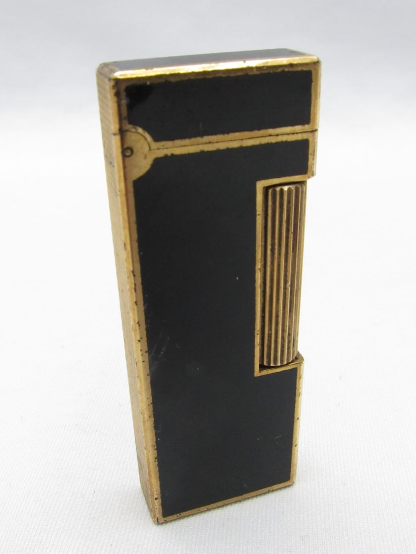 A Metal Lighter Plated in Gold And Black Lacquer Made By Dunhill: A Metal Lighter Plated in Gold And Black Lacquer Made By Dunhill, Switzerland, signed and numbered on the bottom, dimensions: 2.5X0.7X6.5 cm. Wear and use marks. According to the owner, all the lighte