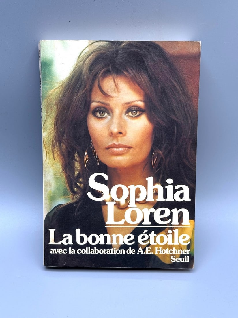 Sophia Loren - Signed Autobiography "La Bonne Etoile": 1979 French edition signed by Sophia Loren in blue pen. Includes a signed B&W postcard dated 1964. Softcover, 286 pages. 20.5 cm. Fair/Good condition: yellowing, small wormhole not affecting text.